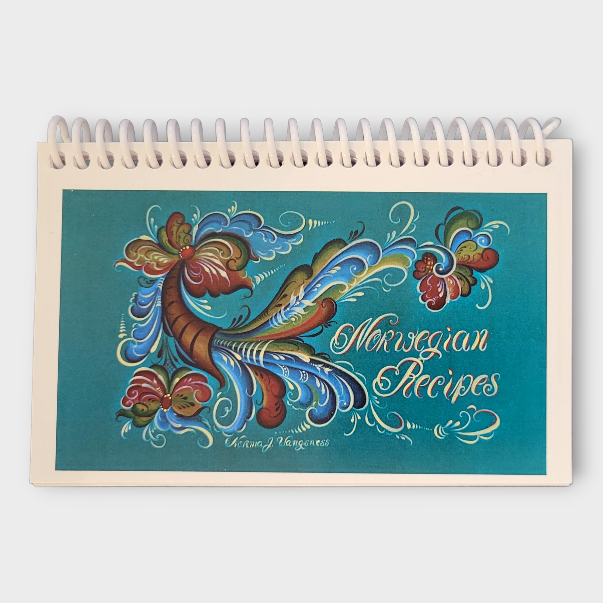 Spiral-bound Book: Norwegian Recipes with a turquoise cover showcasing vibrant floral artwork, ideal for discovering traditional dishes such as lefse.