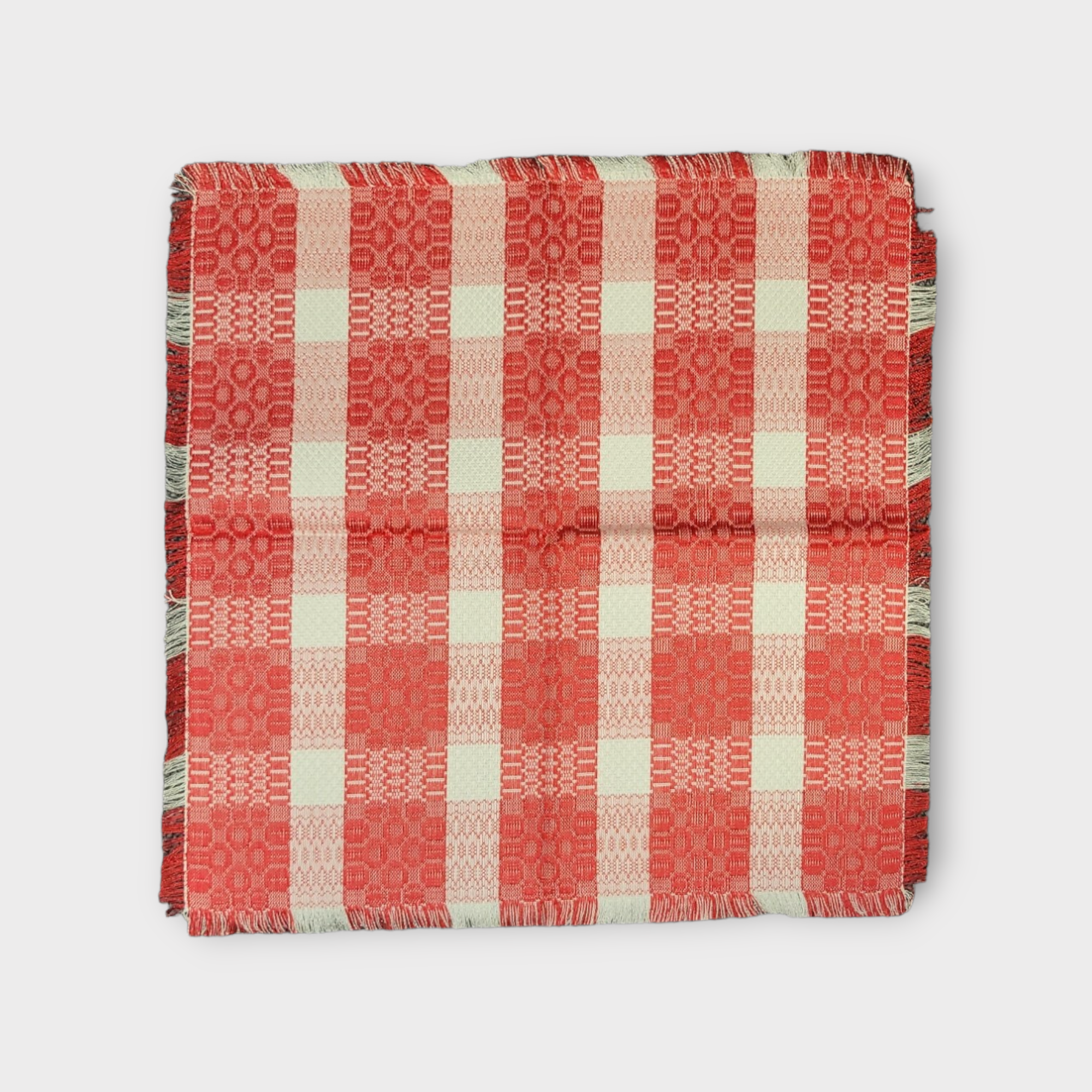 The Placemat: 18" Red/White Square, featuring a textured red and white checkered cotton design, neatly folded on a white background, introduces vintage elegance to your dining table.