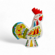 Introducing the Dala Rooster: White, a vibrant ceramic piece adorned with intricate patterns in bright reds, blues, and greens. Set against a plain white background, this exquisite rooster embodies the art of Swedish traditional handcraft through its expertly hand-carved and painted details.
