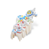 A set of five hand-carved Dala Horses, named White Base with Multi-Color Trim Swedish Dala Horse, arranged from smallest to largest, showcases their colorful painted designs.