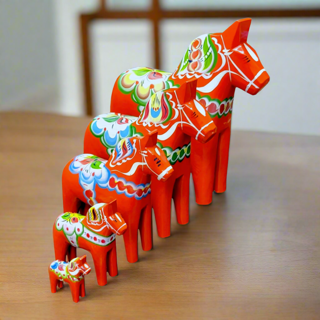 Five hand-carved Red Swedish Dala Horses, handcrafted from pine in various sizes, are displayed on a wooden surface, highlighting the charm of Swedish folk art.