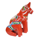 The Sitting Red Dala Horse – Hand-Carved Swedish Figurine features vibrant folk art patterns in green, white, yellow, and blue, exemplifying traditional Swedish charm.