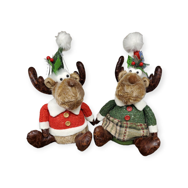 The Dapper Girl Moose Gnome, wearing a green Christmas dress, festive hat, and white pom-poms, sits alongside another moose against a white background.