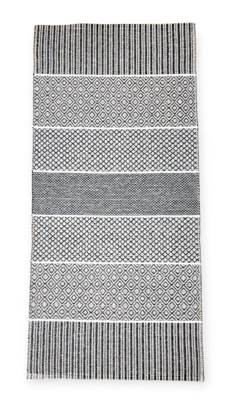 The Horredsmattan Alfie Graphite vinyl rug showcases a black and white pattern with alternating geometric stripes and diamond shapes, combining stylish design with sustainability thanks to its eco-friendly materials.