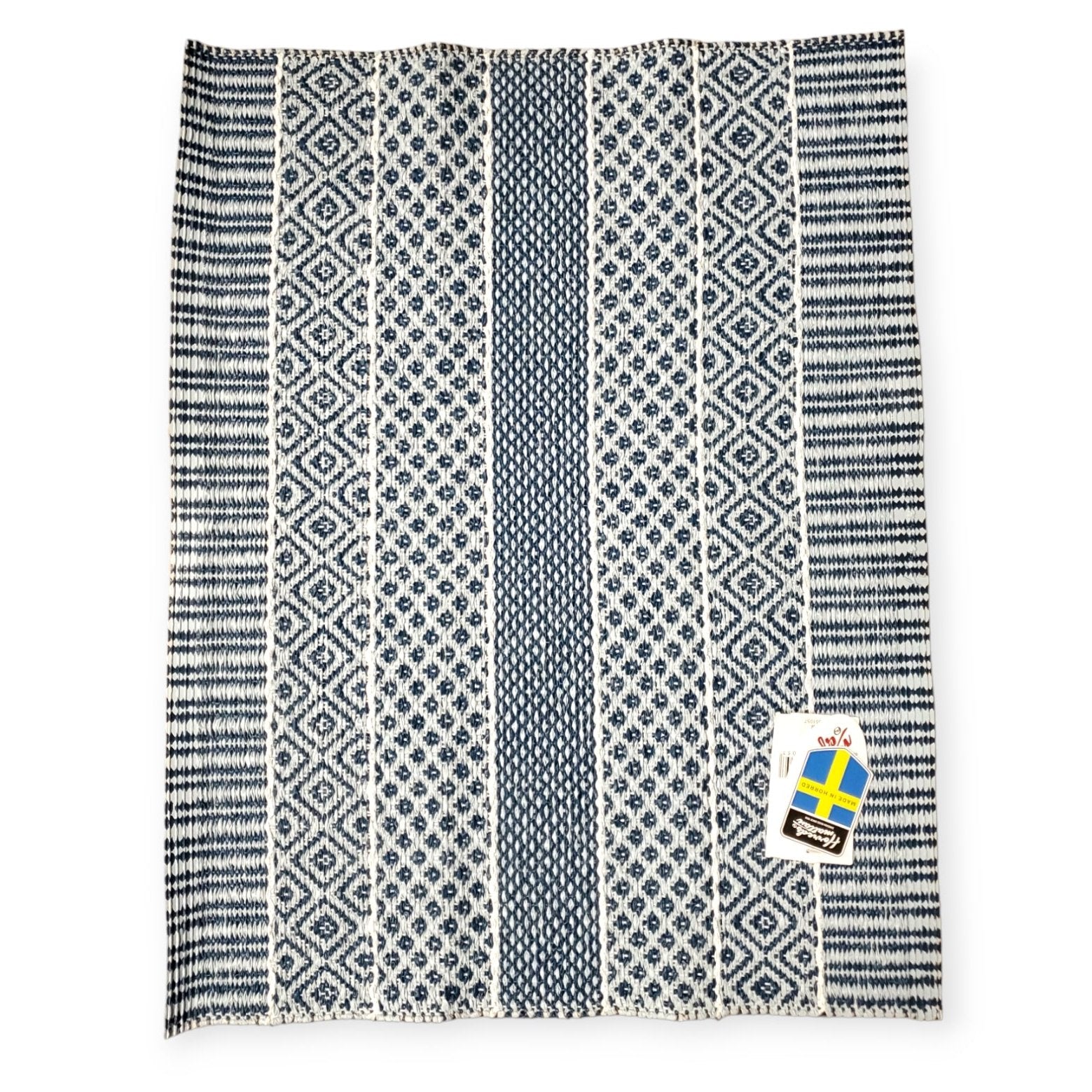 The Rug: Alfie Blue is a blue and white patterned textile made from woven plastic vinyl, featuring a Swedish flag tag in the corner, reminiscent of a classic Horredsmattan design.