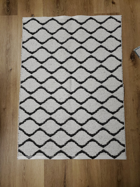 The Rug: Wave Black, a rectangular Swedish vinyl rug featuring a black wavy line pattern, adds durable and long-lasting appeal to a wooden floor.