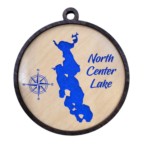 A handcrafted round wooden ornament, etched with a blue map outline of North Center Lake and featuring a compass rose alongside the text "North Center Lake," encapsulates the spirit of adventure and nature in one charming piece.
