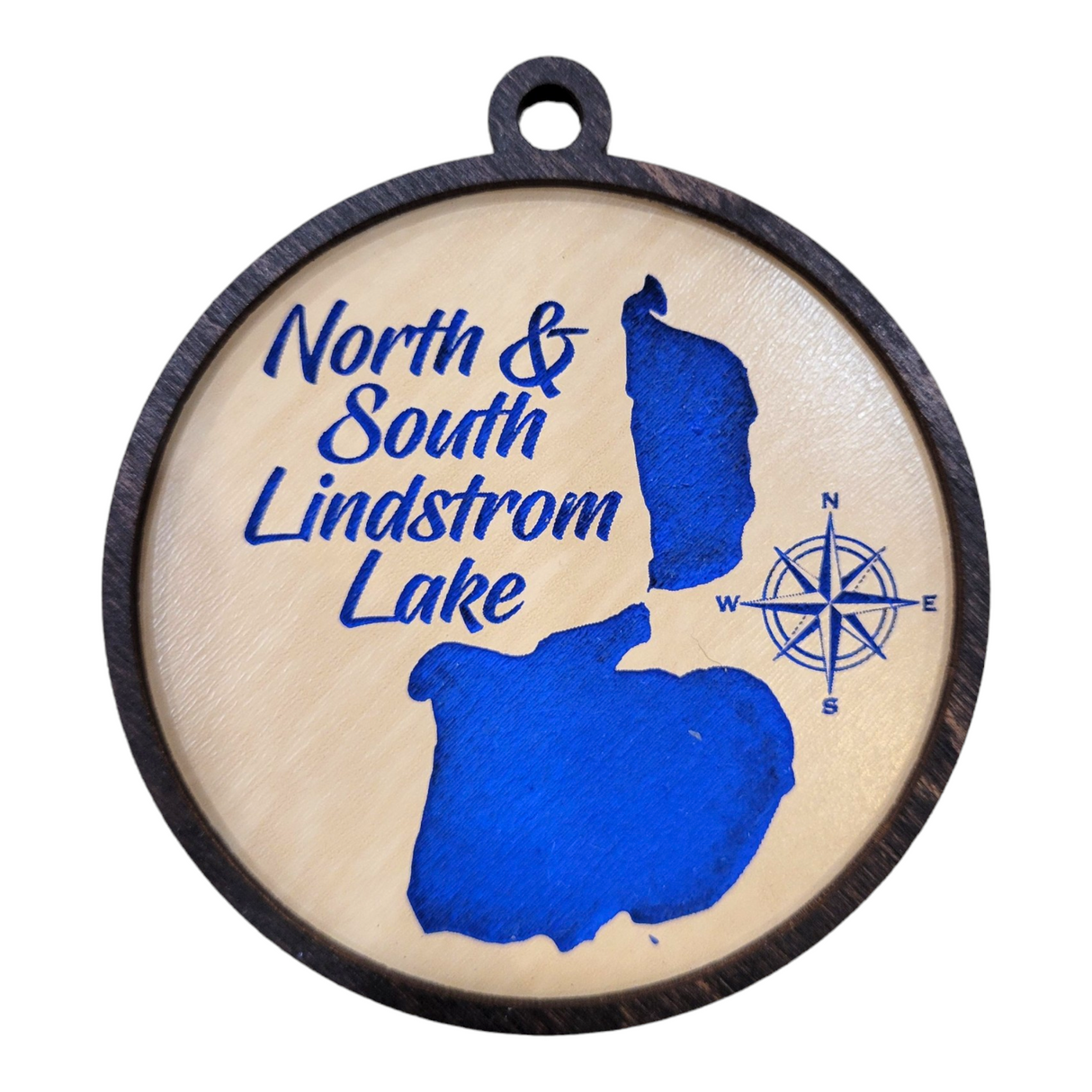 Lake Art: No & So Lindstrom Lake Small is a round wooden ornament featuring blue lake shapes, a blue compass rose, and blue text that reads "North & South Lindstrom Lake" on a light background.