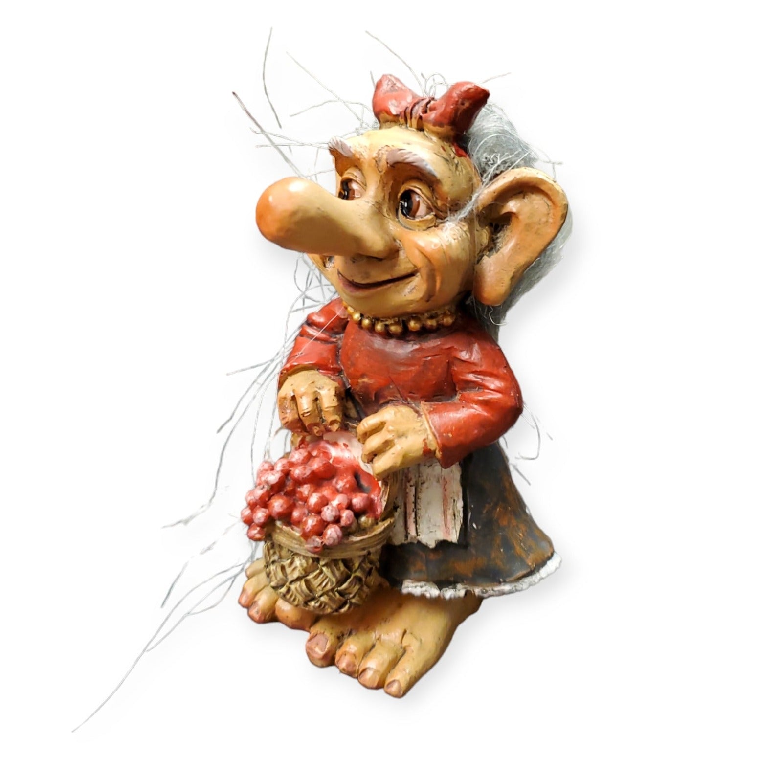 The Troll: Troll w/Lingonberries is a whimsical figurine featuring large ears and dressed in a charming Norwegian red dress, while holding a basket filled with plump lingonberries.