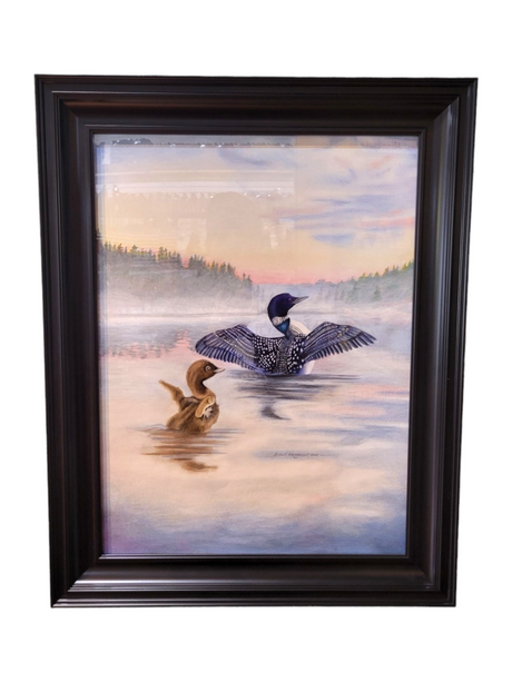 A 23x29 framed piece titled "Loon - Greet the Morning," showcasing a loon with open wings on a serene lake that mirrors the Minnesota wilderness, complemented by a duckling set against a forested backdrop under a vibrant sky.