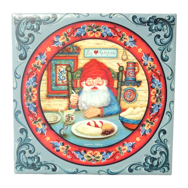 The Tile: Santa Eats Lutefisk 6" Tile with Norwegian Rosemaling features a festive illustration of Santa Claus savoring lutefisk, surrounded by ornate borders in the traditional Norwegian Rosemaling style and a sign saying God Julefest, embodying the spirit of a Scandinavian Christmas.