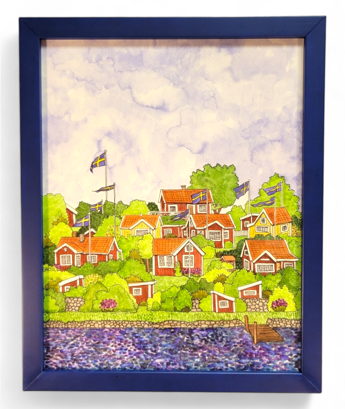 Artwork titled "Brändaholm" by Greta Lann, featuring a framed painting of a scenic village adorned with red and white houses, Swedish flags, lush greenery capturing the essence of Karlskrona's Brändaholm charm, and a calm body of water in the foreground.