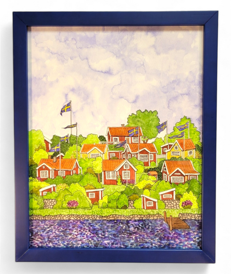 Artwork titled "Brändaholm" by Greta Lann, featuring a framed painting of a scenic village adorned with red and white houses, Swedish flags, lush greenery capturing the essence of Karlskrona's Brändaholm charm, and a calm body of water in the foreground.