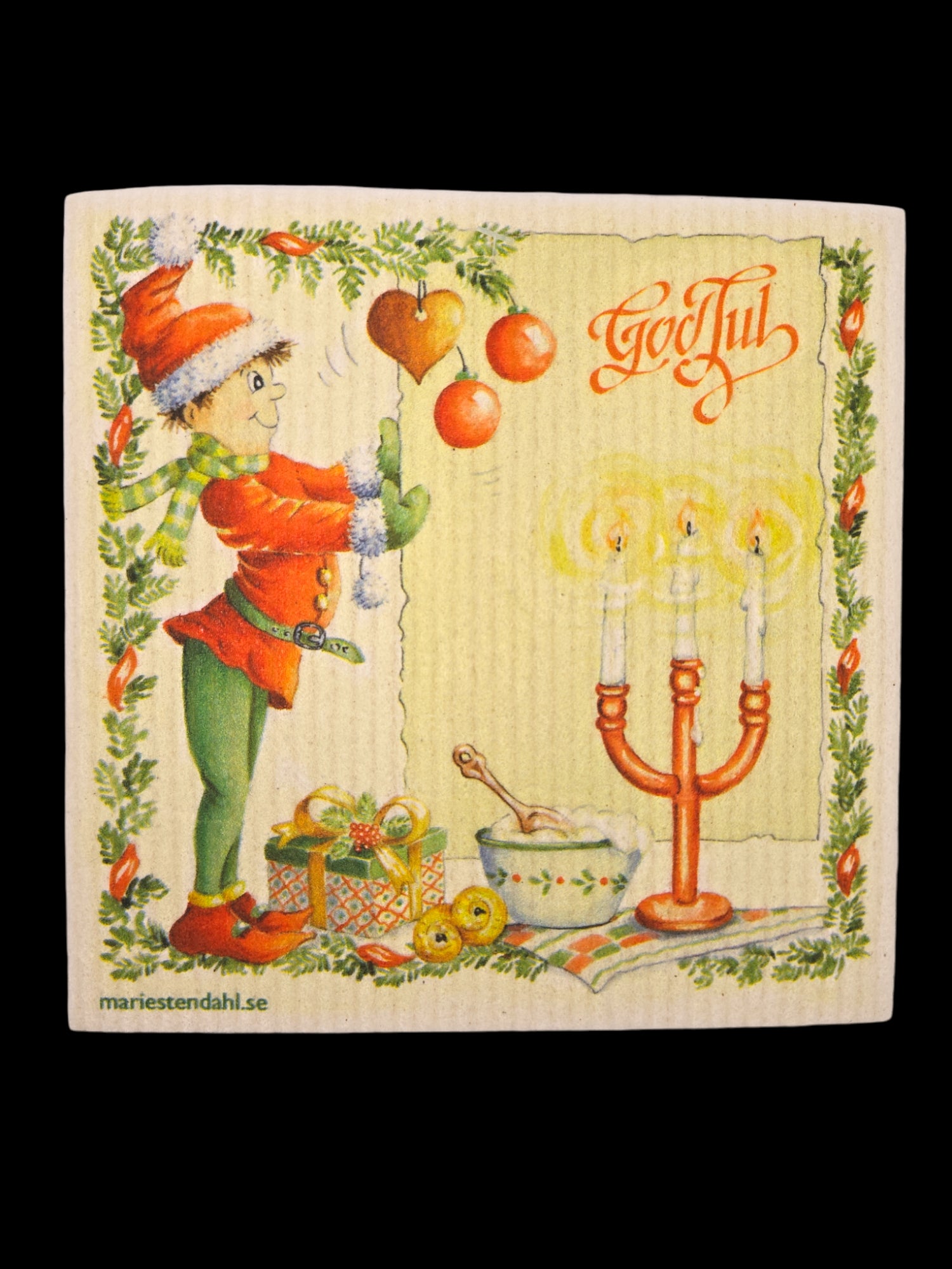 A festive elf decorates a tree with red hearts, surrounded by gifts and glowing candles, while a Swedish dishcloth featuring the text "God Jul," designed by Marie Stendahl, is draped over a mixing bowl.