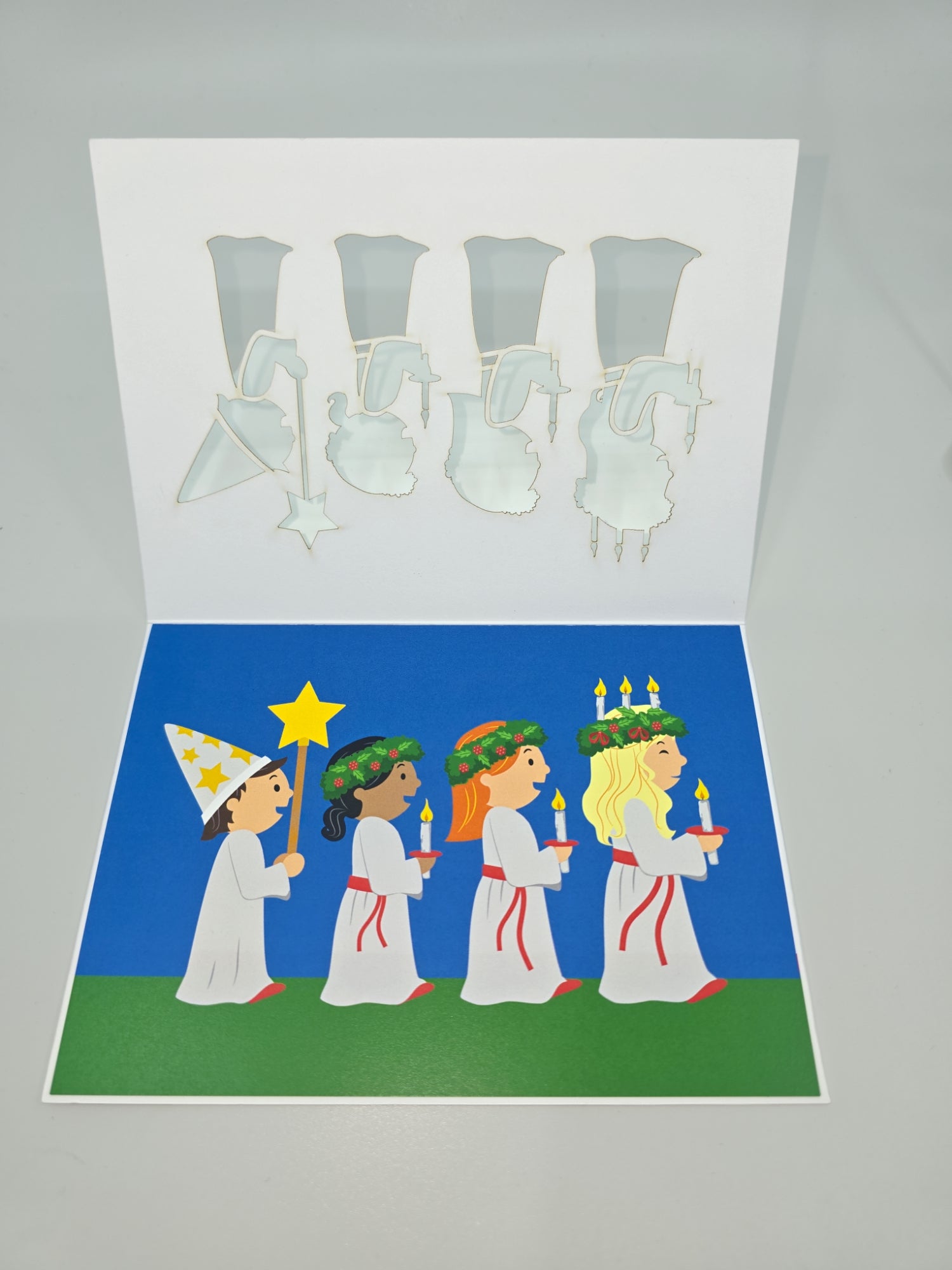 A pop-up card from the "Cards: St Lucia" collection, featuring four children in white robes and candle headpieces walking in a line to celebrate St Lucia Day with lit candles, surrounded by intricate illustrations of Swedish birds and flowers.