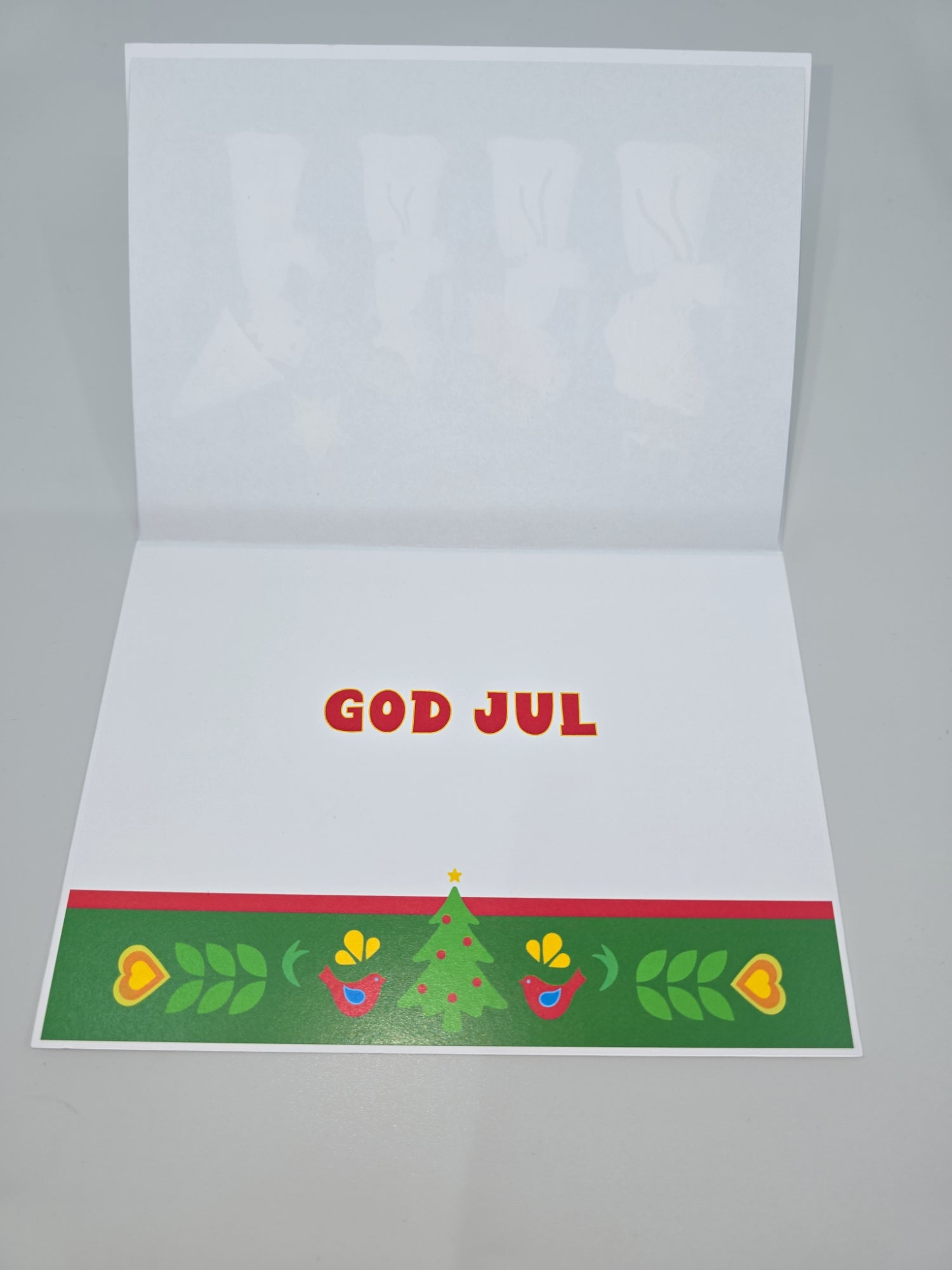 An open Cards: St Lucia greeting card displays the text "God Jul," encircled by Christmas decorations such as a tree, vibrant hearts, and leaves, capturing the essence of St Lucia Day. Delicate Swedish birds and flowers subtly enhance this enchanting festive scene.