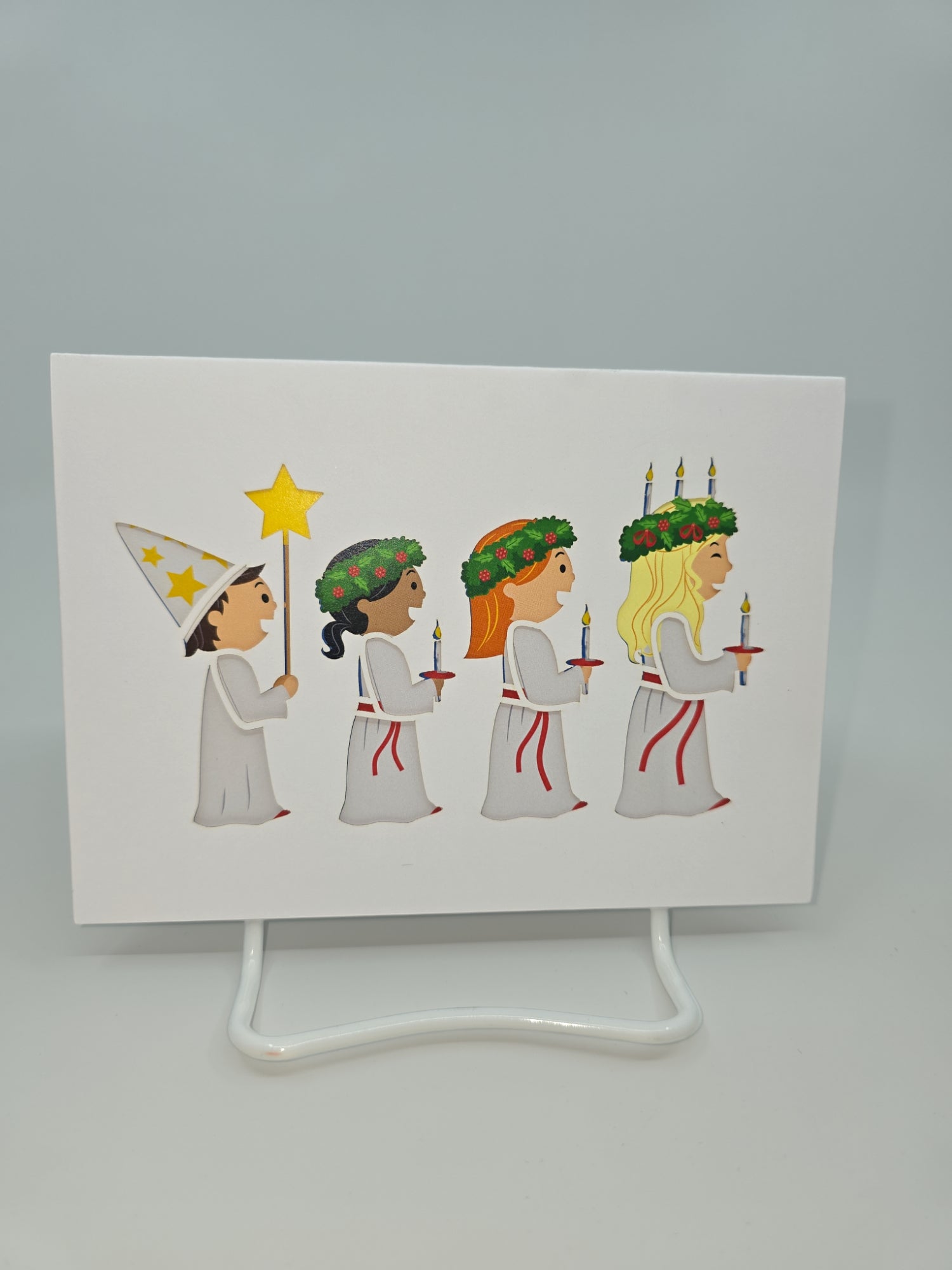 A depiction from the "Cards: St Lucia" collection shows four children in white robes, each holding candles in celebration of St Lucia Day. One child is adorned with a pointed hat, while the others wear wreaths with candles, perfectly capturing the essence of this Swedish festival of lights.