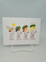 A depiction from the "Cards: St Lucia" collection shows four children in white robes, each holding candles in celebration of St Lucia Day. One child is adorned with a pointed hat, while the others wear wreaths with candles, perfectly capturing the essence of this Swedish festival of lights.