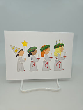 A depiction from the "Cards: St Lucia" collection shows four children in white robes, each holding candles in celebration of St Lucia Day. One child is adorned with a pointed hat, while the others wear wreaths with candles, perfectly capturing the essence of this Swedish festival of lights.