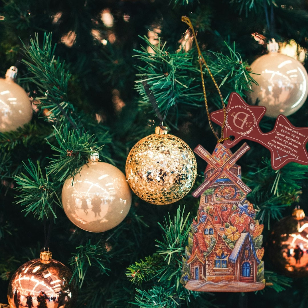 A Christmas tree adorned with gold and cream baubles features a charming Danish windmill magnet ornament. Among the decorations are handcrafted wooden ornaments from the G.DeBrekht art studio, adding a touch of Santa Around the World magic to the festive scene.