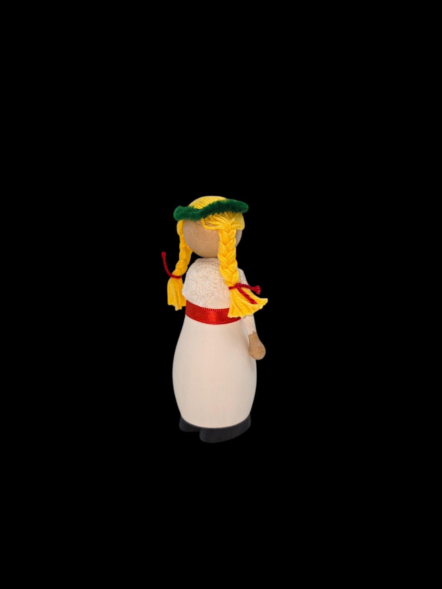 The St Lucia Hand-crafted Wood Figurine, standing 4 inches tall, features braided yellow hair, a green hat, and a red ribbon around its waist. Set against a black background, it beautifully evokes the spirit of St Lucia while embodying the timeless tradition of Christmas holidays.