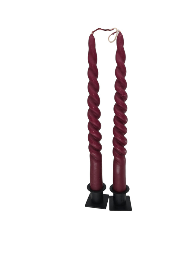 Two Twisted Burgundy Taper Candles (2) from Logum Kloster Denmark stand upright in black square holders against a white background.