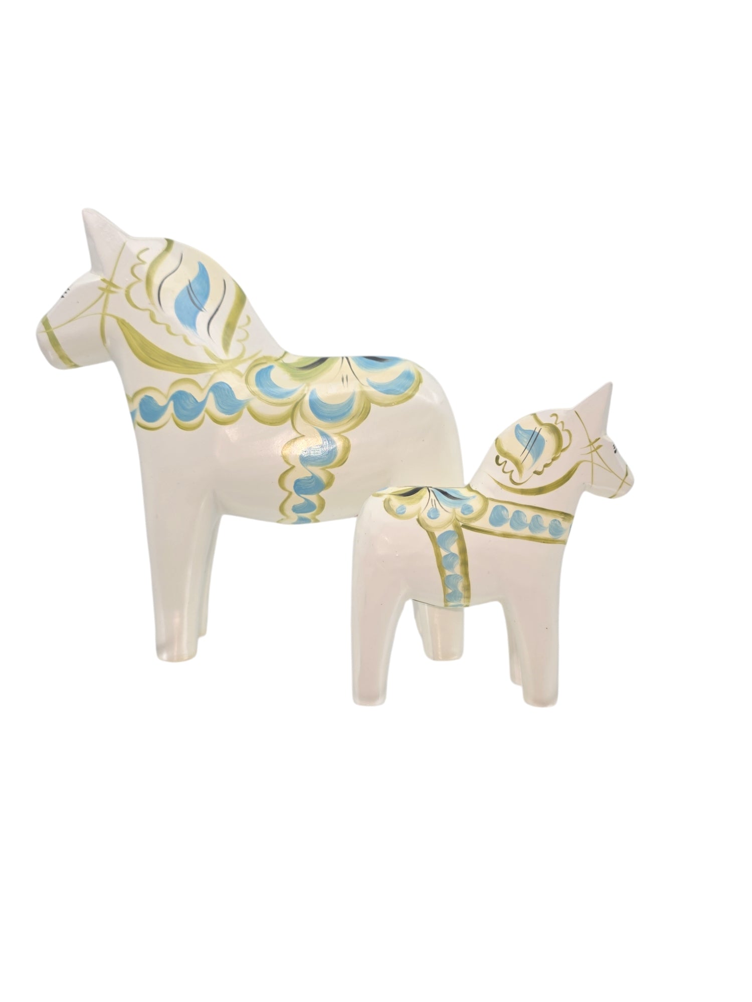 The Dala Horse: Pastel on White Swedish Dala Horse with Kurbits showcases two white ceramic horses adorned with intricate green and blue hand-painted patterns. The larger horse stands behind the smaller, both elegantly facing left.