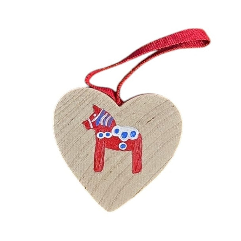 This heart-shaped wood ornament features a red Swedish Dala Horse with blue and white details and comes with a red hanging ribbon. Handcrafted in Sweden.