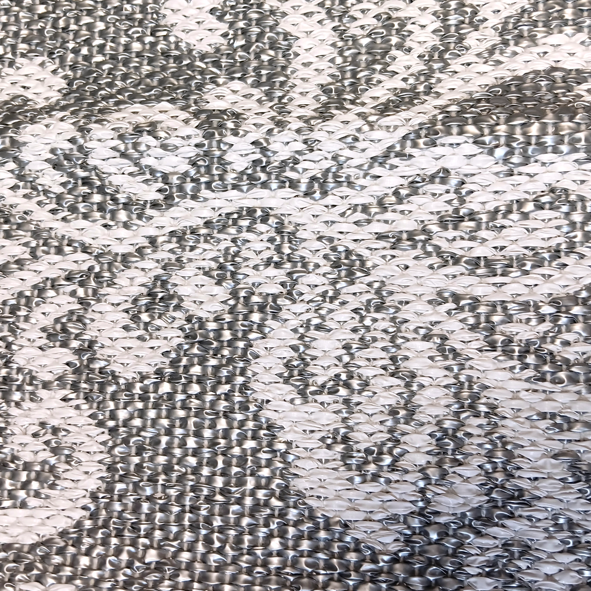 A close-up of the Swedish Grey Kurbits Rug showcases an abstract kurbits pattern on a textured silver surface, highlighted by swirling shapes and raised dots.