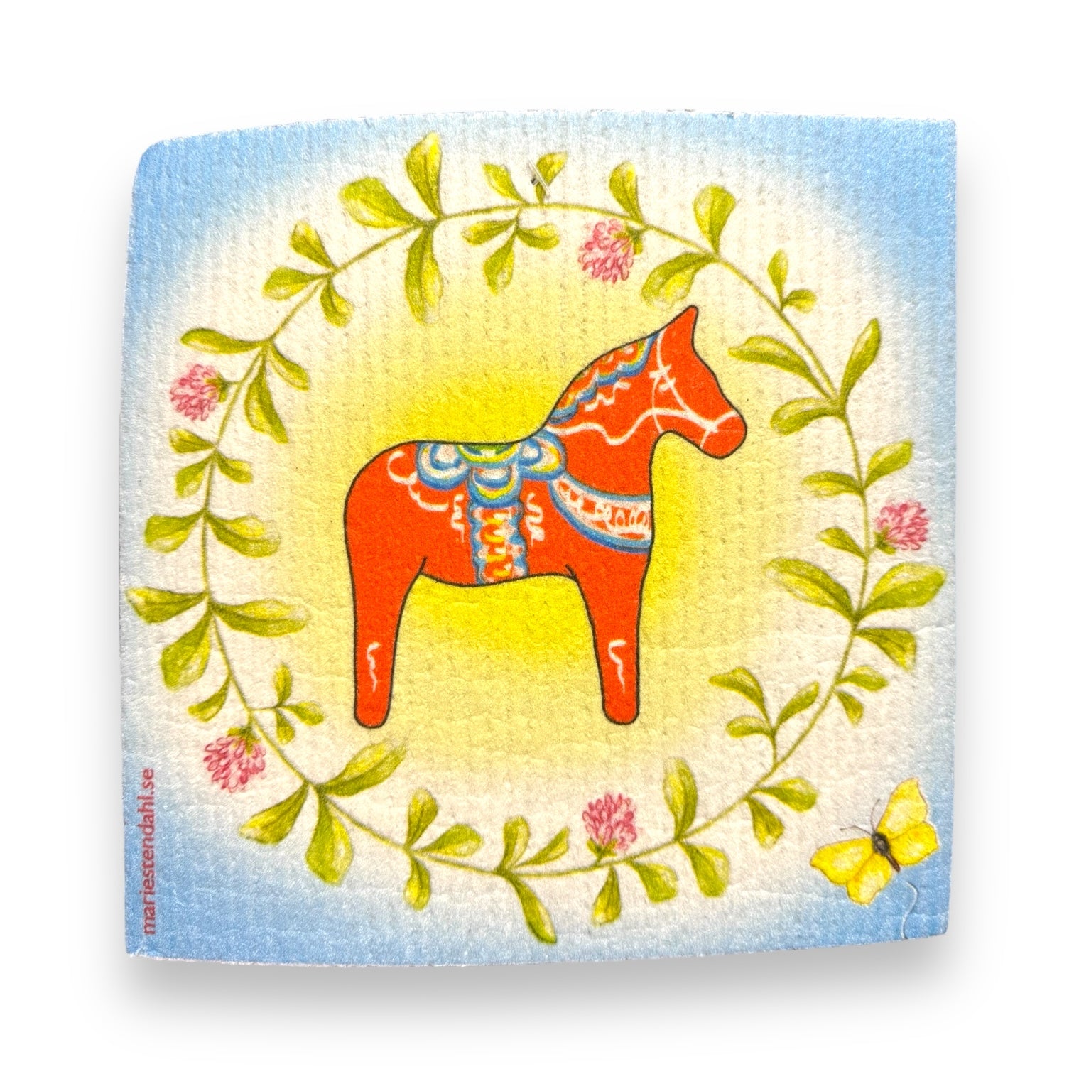 Illustration of a red Dala horse encircled by a lush green clover wreath, accented with pink flowers, all set on a softly transitioning light blue background. A yellow butterfly flits in the bottom right corner, enhancing the eco-friendly allure and utility provided by the "Dish Cloth: Dala Horse with Clover Wreath" designed by Marie Stendahl.