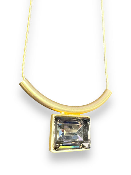 The Audrey Black Diamond Gold Plated Necklace by DANSK Copenhagen features a minimalist curved bar and a large rectangular clear gemstone pendant, embodying Nordic design.