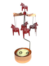 The Candle Holder: Red Dala Horses with Rose-Gold Color Candle Holder & Spinner by Pluto Design features horse-shaped ornaments that spin above a round base, inspired by classic Swedish rotary candle holders.