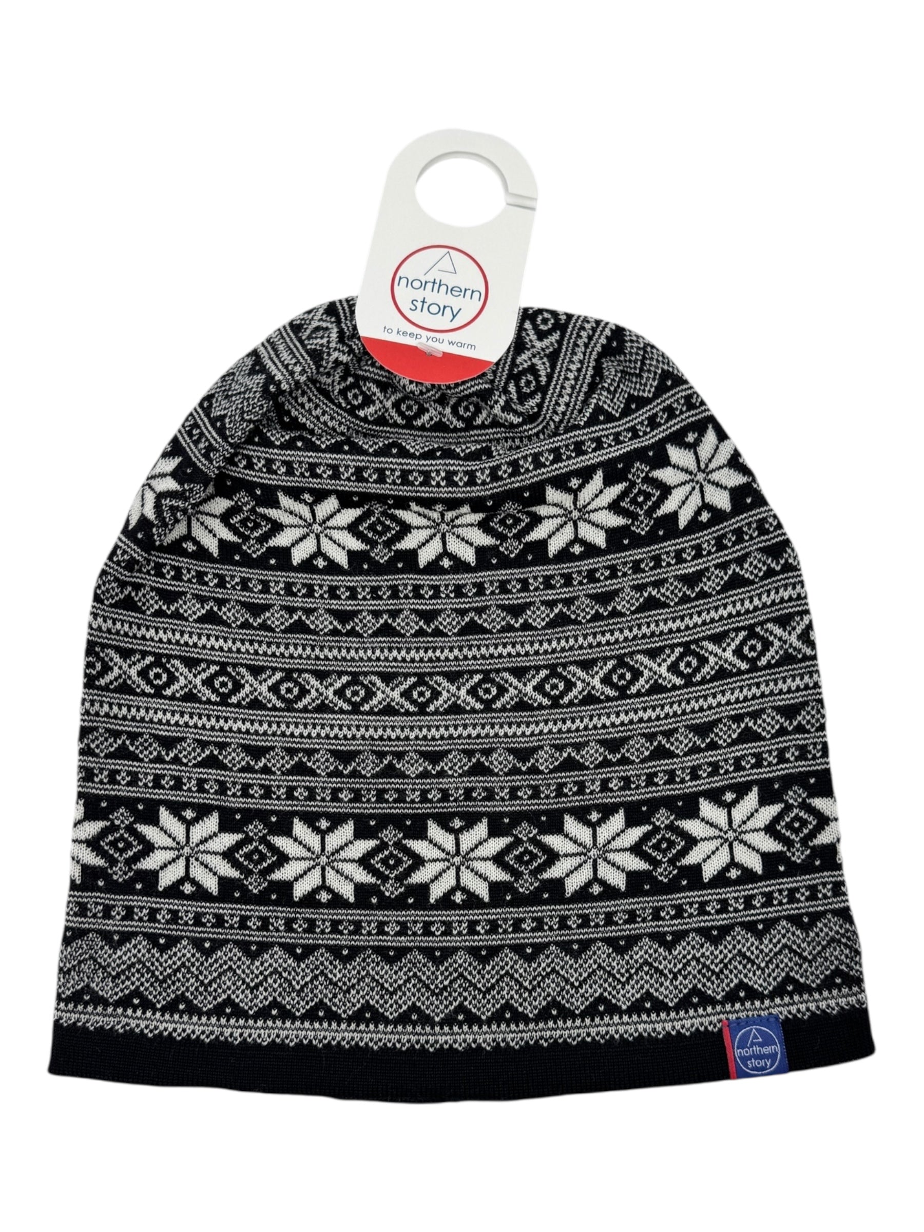 The Northern Story Setesdal Hat is a black and white knit beanie with a Selbu star pattern, made from 100% soft merino wool, and finished with a branded tag attached at the top.
