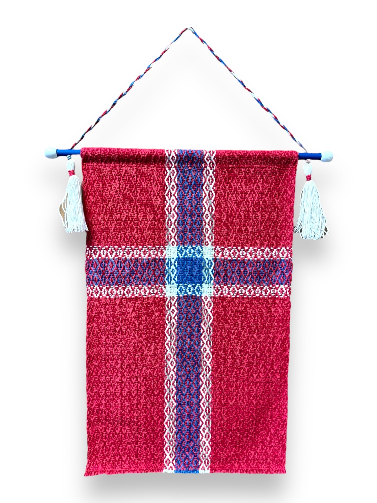 The Flag: Flag on Hanger - Norway is a red hand-woven wall hanging adorned with a blue and white cross pattern that resembles the Norwegian flag. It boasts decorative tassels at the top corners and is elegantly hung from a blue rod, highlighting craftsman skills reminiscent of an antique loom's charm.