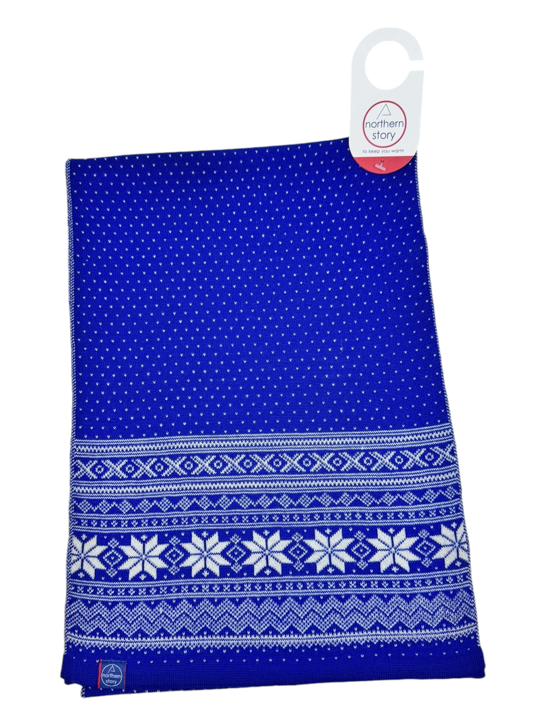 A Northern Story Cardigan Setesdal Royal Blue scarf with a white snowflake and geometric pattern, hanging from a cardboard tag. Made from soft lamb's wool, it showcases an exquisite Norwegian design that combines classic elegance and warmth.