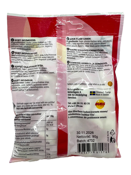Back of Bubs Goody - Sour Vanilla Strawberry Ovals (90g) package with multilingual text, nutrition facts, Fairtrade-Certified Sugar in ingredients, barcode, expiration date, manufacturer info. Features vegan-friendly sour vanilla strawberry flavor.