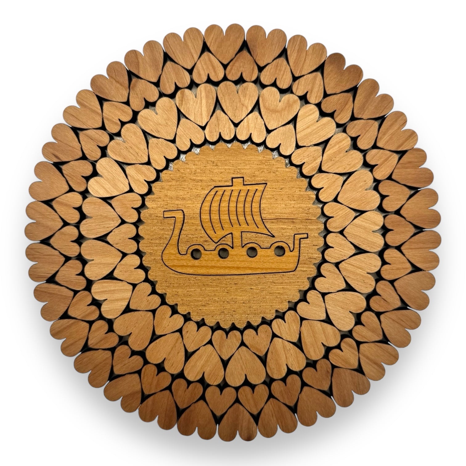 The Trivet: Viking Ship with Hearts (6) is handmade from alder in Estonia, featuring a central Viking ship engraving surrounded by concentric circles of heart-shaped wood pieces.