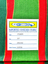 Close-up of the imported Swedish fabric label from the Runner: Julrand Holiday Runner, featuring a cotton table runner with a festive green and red stripe pattern. The label details include size (36), color (striped), and luxurious cotton fabric content.