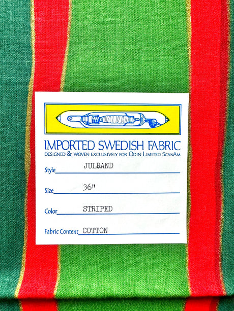 Close-up of the imported Swedish fabric label from the Runner: Julrand Holiday Runner, featuring a cotton table runner with a festive green and red stripe pattern. The label details include size (36), color (striped), and luxurious cotton fabric content.