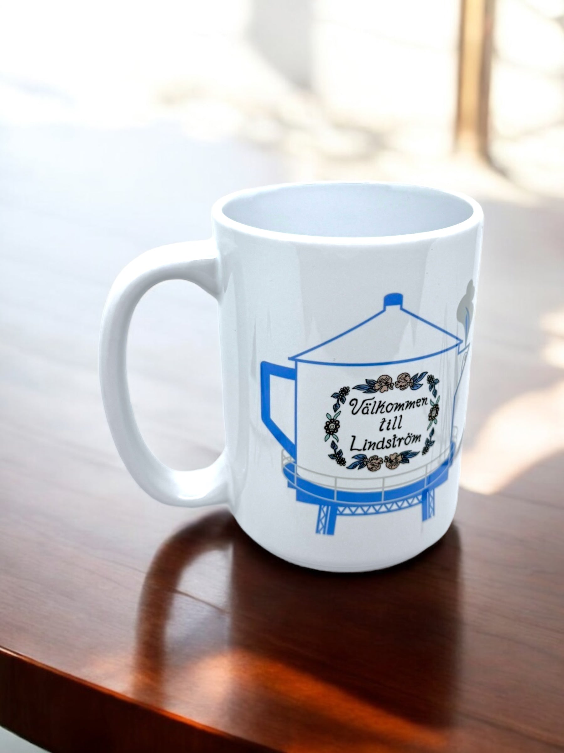 The 15oz Valkommen to Lindström Swedish Coffee Pot Water Tower Mug features the Lindström Water Tower, “Välkommen till Lindström” text, and a floral wreath—perfect for celebrating Americas Little Sweden.