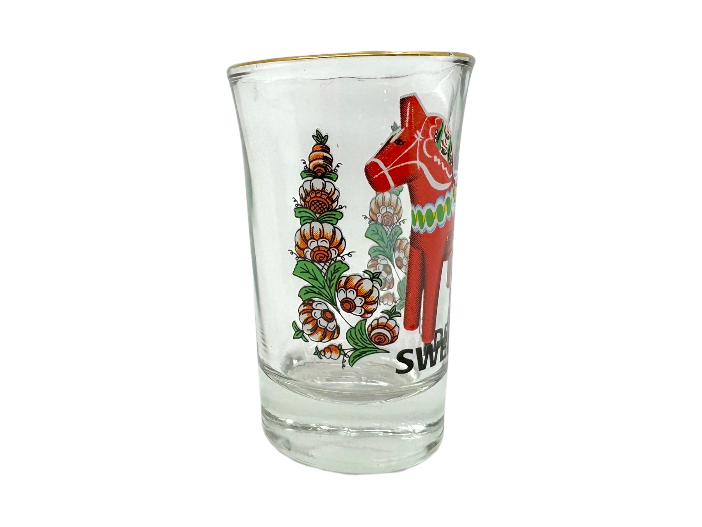 The Shot Glass: Sweden Red Dala Horse showcases a Scandinavian folk art design with a red Dala horse and floral motifs, plus Sweden near the base—making it a vibrant Nordic souvenir.