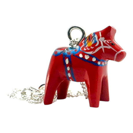 The Red Dala Horse Necklace features a 2cm handcrafted pendant inspired by Swedish Folk Art, painted in blue, yellow, and white, on a 19 sterling silver chain.