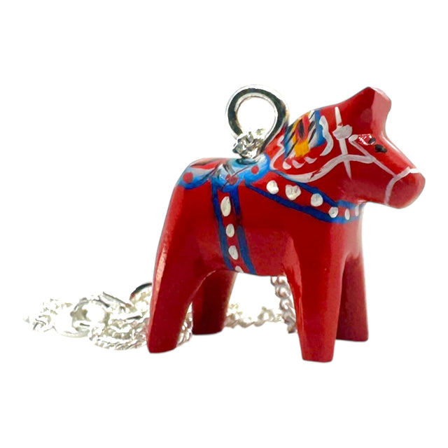 The Red Dala Horse Necklace features a 2cm handcrafted pendant inspired by Swedish Folk Art, painted in blue, yellow, and white, on a 19 sterling silver chain.