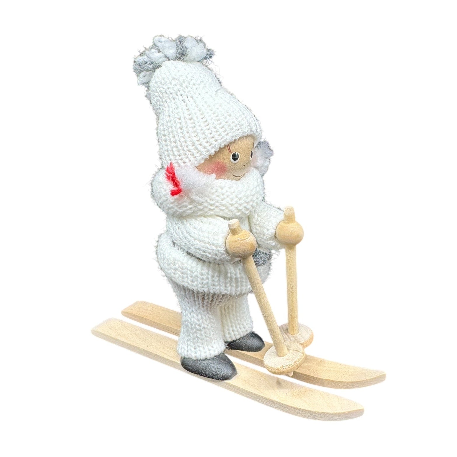 The Figurine: Scandinavian Girl on Skis with White Snow Suit features a handmade design of a girl dressed in a white knitted outfit, hat, and mittens, standing on wooden skis and holding ski poles.
