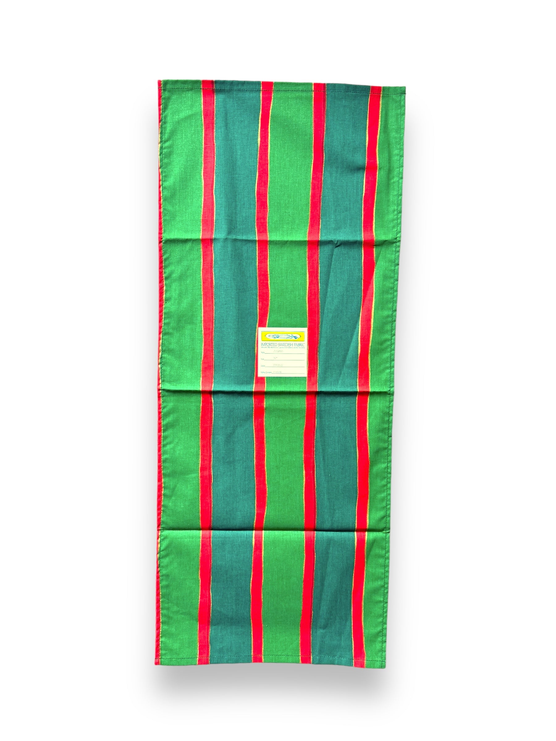 A rectangular cotton table runner, named the Julrand Holiday Runner, featuring vertical green, red, and blue stripes with a label centered on it.