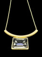 The Necklace: Audrey Black Diamond Gold Plated by DANSK Copenhagen exudes timeless elegance with its minimalist design featuring a curved gold bar, large rectangular gem, and thin chain set against a black backdrop. Its simplicity makes it a versatile accessory for any occasion.