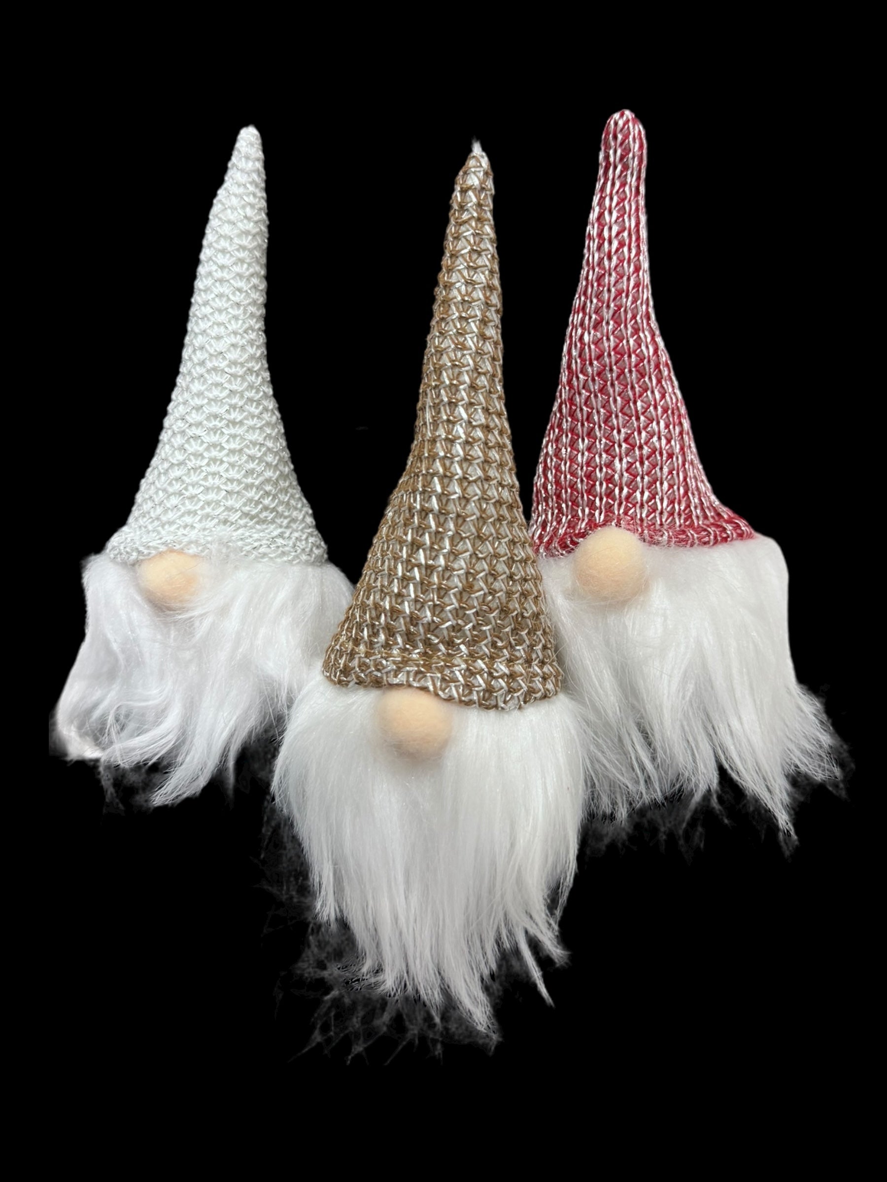 The Ornament: Light Up Tomte Gnome features three charming figurines adorned with knitted hats in white, brown, and red. Each of these gnomes has a long, white beard and is battery-operated, set against a black background. These decorations come in three colors and include A76 (LR44) batteries.