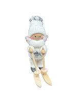 The Figurine: Scandinavian Girl on Skis with White Snow Suit depicts a handmade girl in a white hat, scarf, and mittens, standing on wooden skis and holding ski poles.