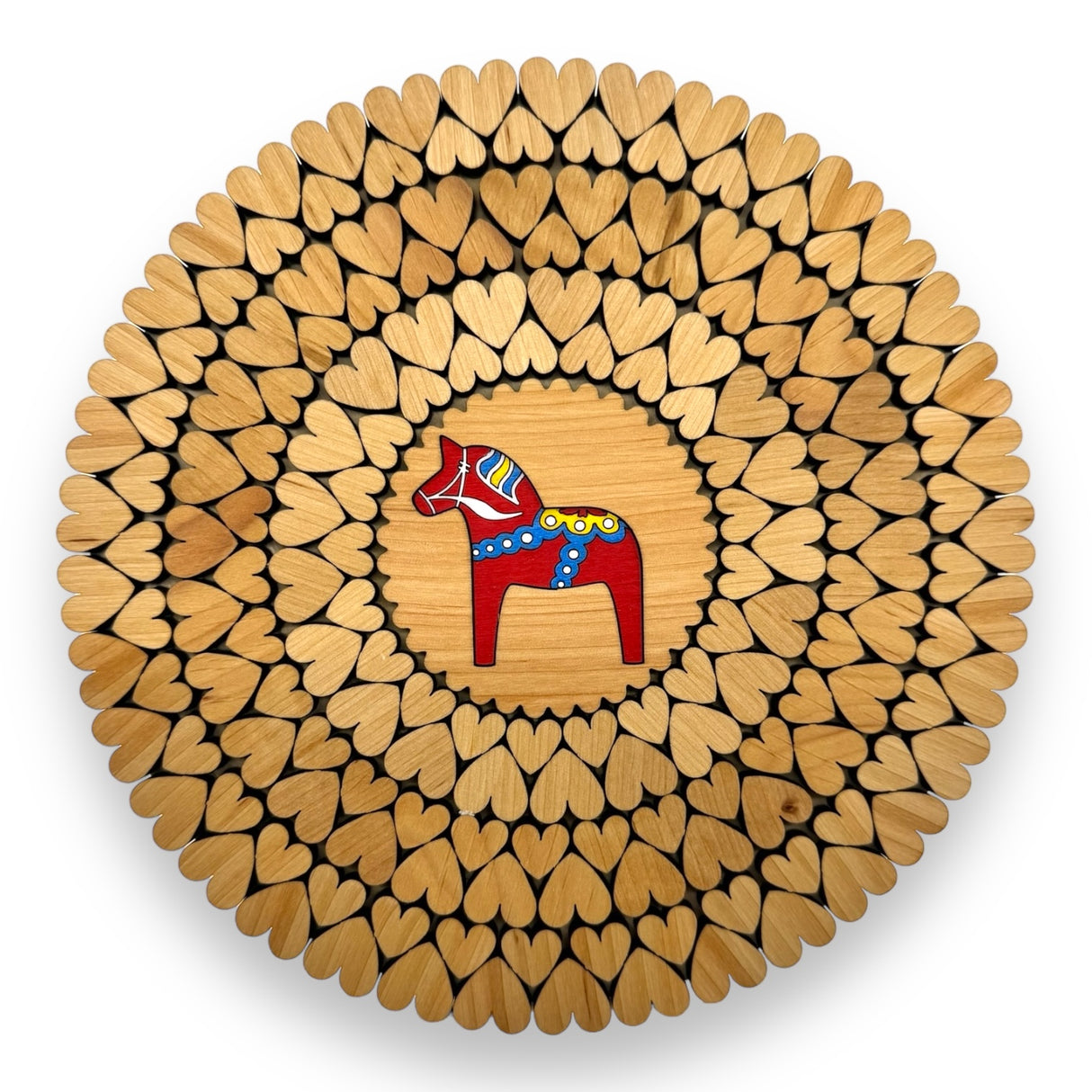 An 8" alder wood trivet features a red Swedish Dala horse at the center, surrounded by laser-cut heart shapes. This handmade piece from Estonia is displayed from above on a white background.