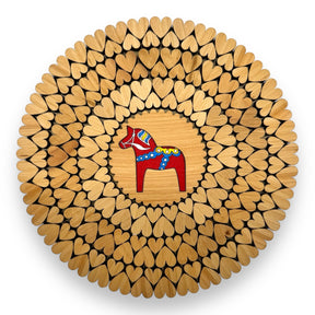 An 8" alder wood trivet features a red Swedish Dala horse at the center, surrounded by laser-cut heart shapes. This handmade piece from Estonia is displayed from above on a white background.